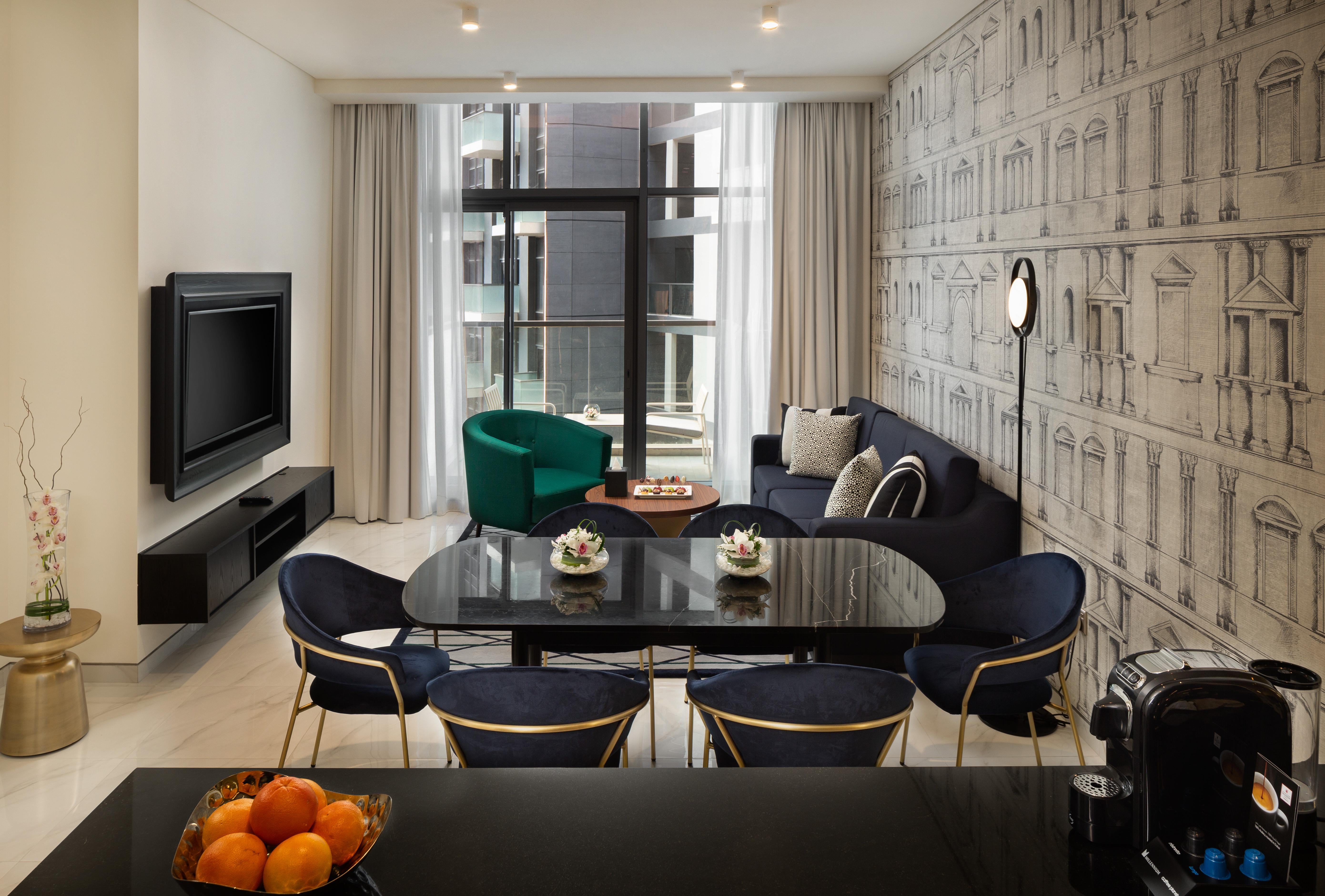 Millennium Atria Business Bay Aparthotel Dubaj Kültér fotó The photo shows a modern living space that includes a cozy seating area and dining setup. On the left, there is a large television mounted on the wall. The living room features a blue sofa and a green accent chair, creating a stylish contrast. A smal