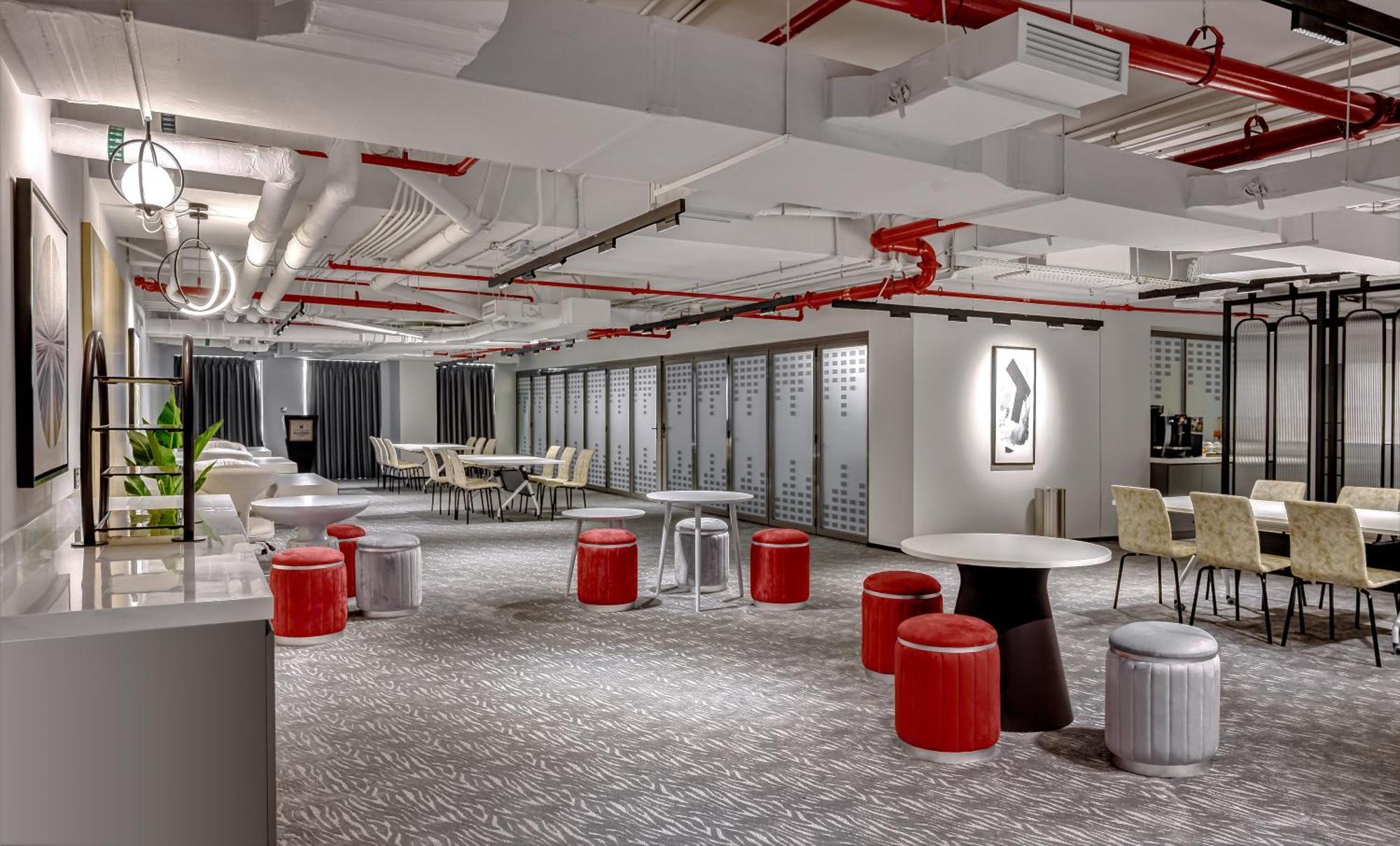 Millennium Atria Business Bay Aparthotel Dubaj Kültér fotó The photo shows a modern interior space, likely an office or communal area. The flooring is covered with a textured carpet, and the ceiling features exposed pipes painted red. 

There are several seating options, including small round tables with sto