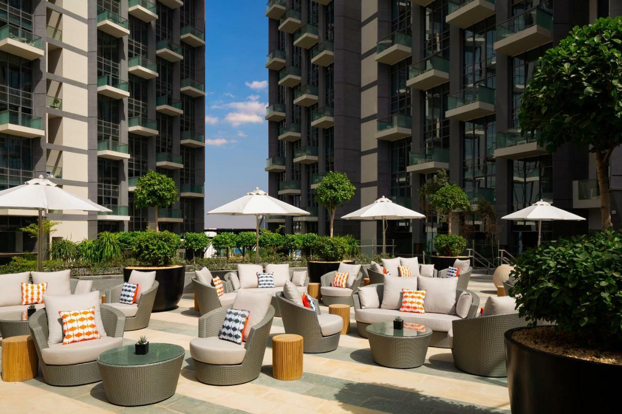 Millennium Atria Business Bay Aparthotel Dubaj Kültér fotó The photo shows a modern outdoor lounge area, featuring several comfortable seating arrangements made of soft, stylish lounge chairs and round tables. The seating is adorned with colorful pillows, adding a pop of color to the neutral tones of the fur