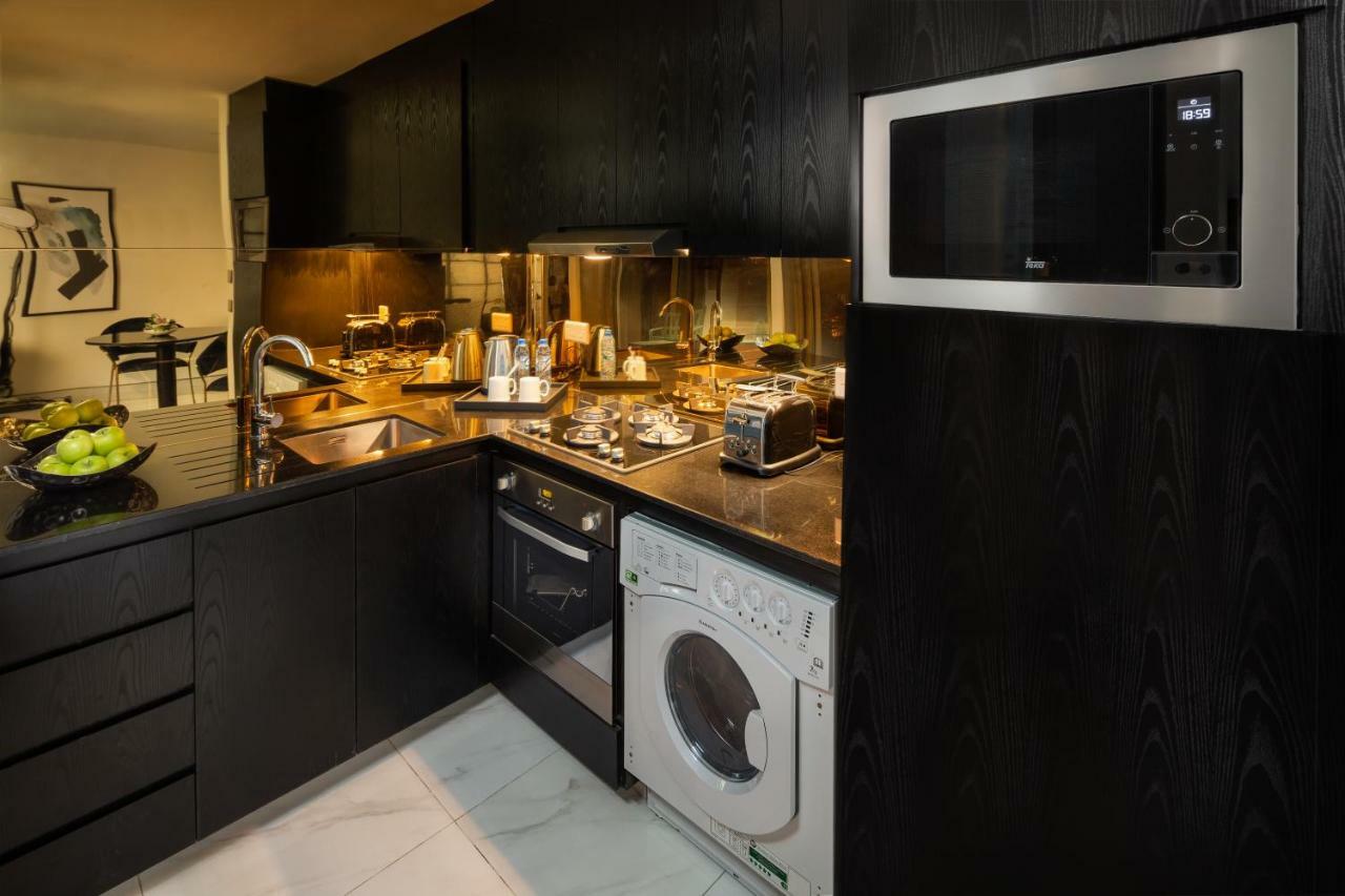 Millennium Atria Business Bay Aparthotel Dubaj Kültér fotó The photo shows a modern kitchen with a sleek design. The cabinets and surfaces are predominantly black, creating a contemporary look. There is a stainless steel microwave mounted above the countertop, and on the counter, various kitchen appliances l