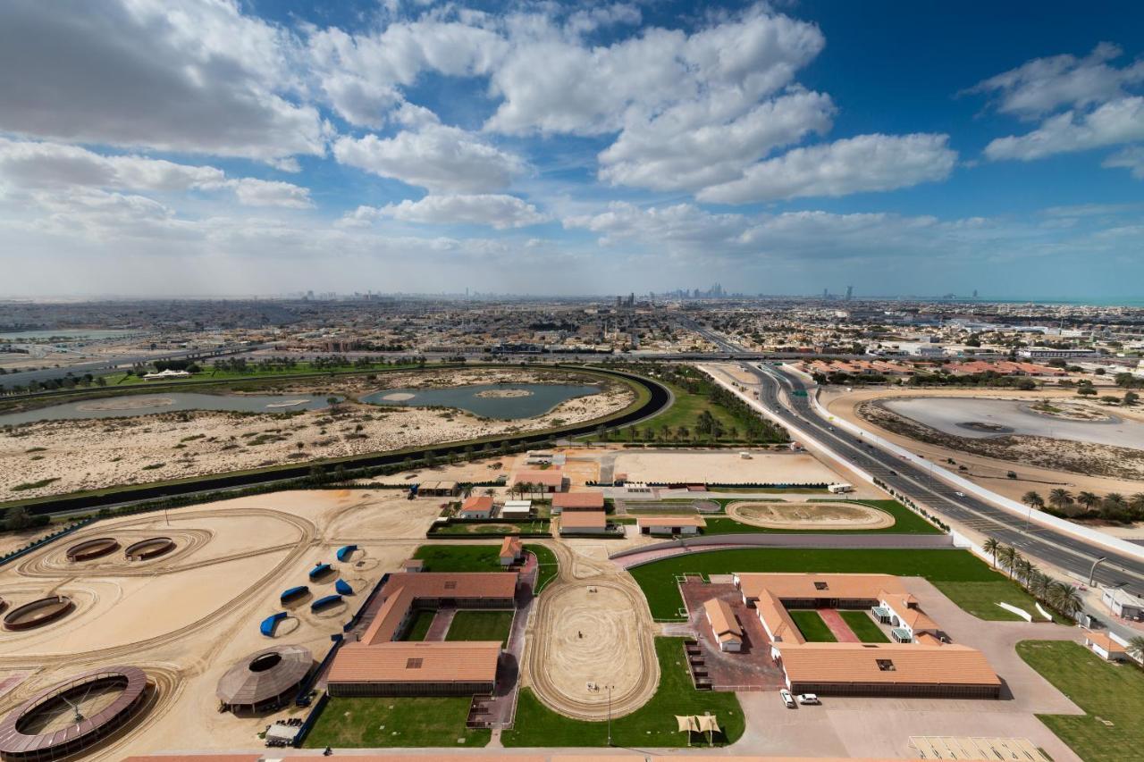 Millennium Atria Business Bay Aparthotel Dubaj Kültér fotó The photo shows a panoramic view of a large landscape with expansive open areas, buildings, and a curved track. In the foreground, there are several stable structures and facilities associated with horse training or racing, surrounded by well-maintai