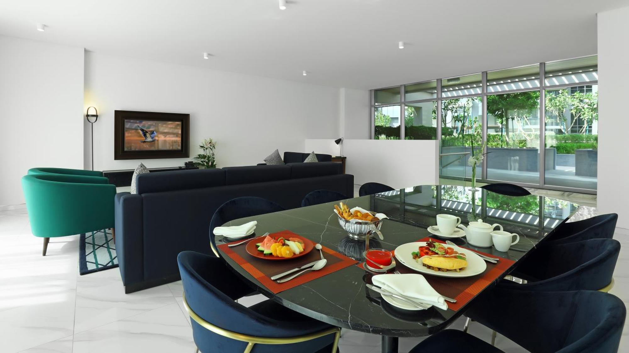 Millennium Atria Business Bay Aparthotel Dubaj Kültér fotó The photo depicts a modern living space with a dining area and a seating area. In the foreground, there is a round dining table set with plates of food, including eggs, toast, and a small bowl of fruit, accompanied by cups and napkins. The table is c